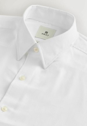 Bijela košulja dugih rukava od glatkog pamuka, s klasičnom kragnom, dva dugmeta na zapinjanju i etiketom s natpisom "NEXT".
