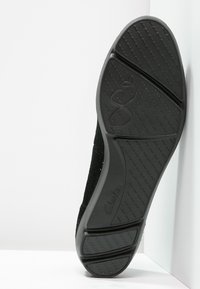 Suela de zapatos de ante negro, con un patrón de agarre texturizado y con marca. El diseño presenta una forma redondeada y ligeramente acolchada.