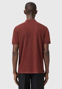 Polo a maniche corte color borgogna con colletto classico, texture morbida e taglio dritto, con fessure laterali sull'orlo.