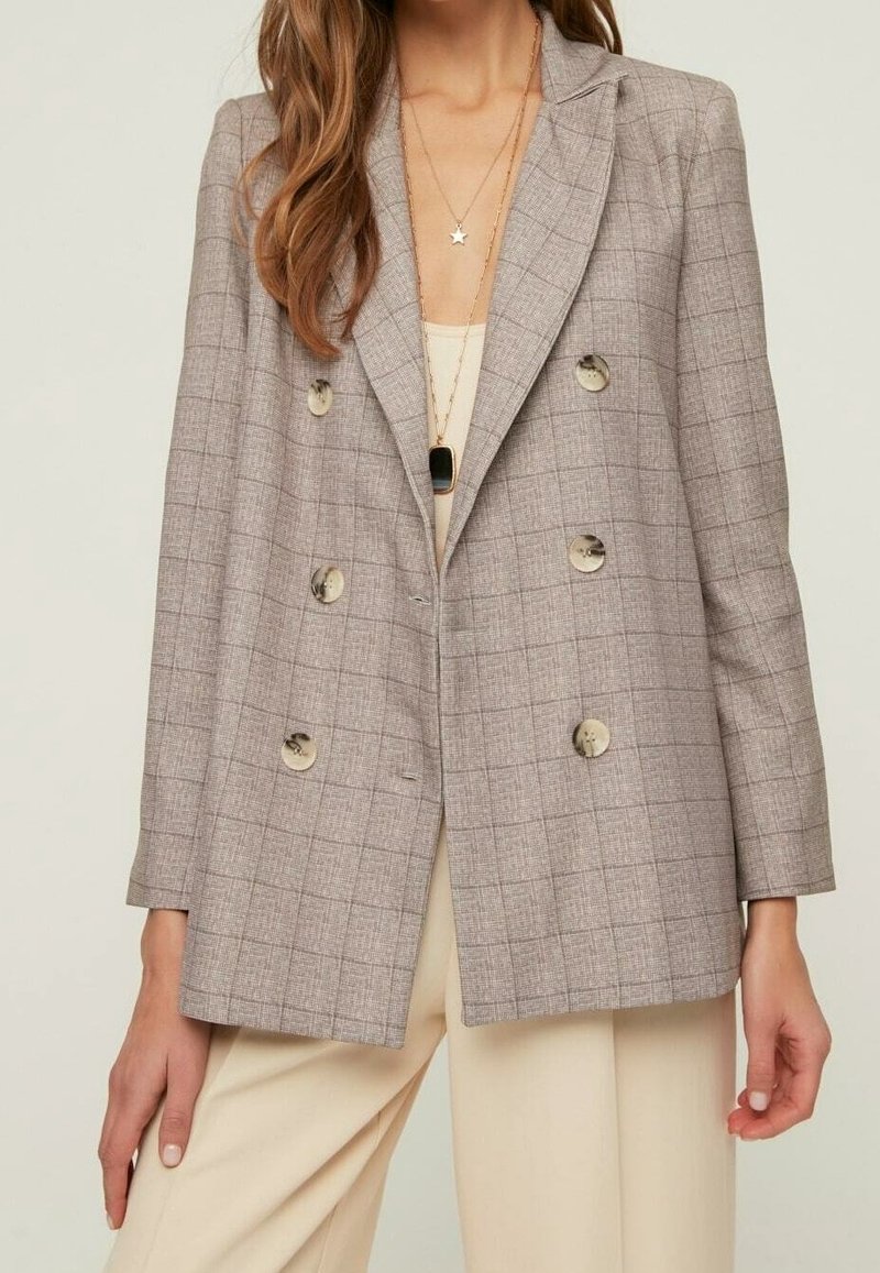 Blazer doppiopetto grigio a quadri con grandi bottoni, rever a lancia e vestibilità sartoriale. Tessuto morbido e forma strutturata con tasche laterali.