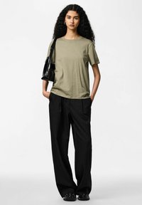 Olivgrön t-shirt med korta ärmar kombinerad med svart kostymbyxa med kritstrecksrand. Modellen håller en glansig svart handväska och visar upp en avslappnad passform.