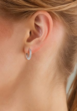 Clou d'oreille en argent avec une finition polie, présentant un design circulaire simple fixé au lobe, reflétant la lumière de manière subtile.