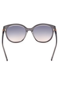 Gafas de sol estilo gato con un marco gris translúcido y lentes degradados. Acentuadas con herrajes en color dorado en la varilla.