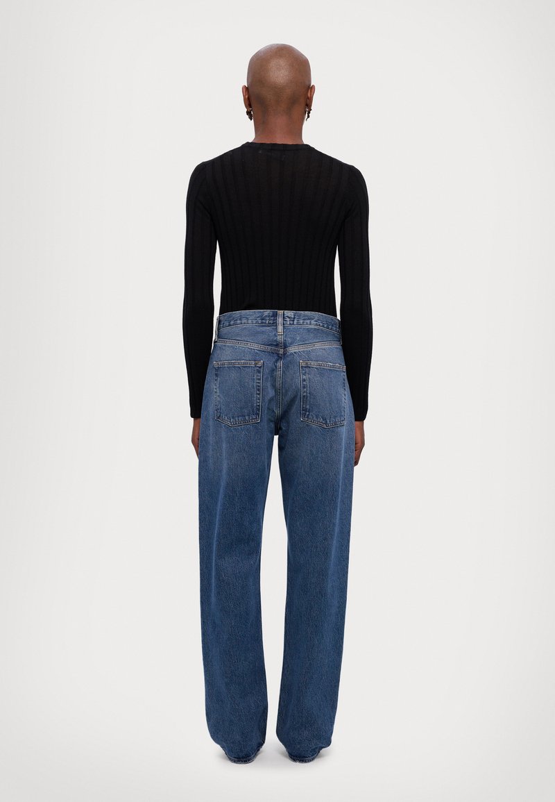 Zwart geribbeld langmouwtopje gecombineerd met blauwe wijde denim jeans, met een hoge taille en twee achterzakken.