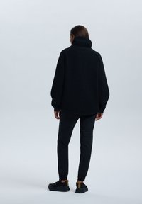Czarny oversize polarowy polar z wysokim kołnierzem, teksturowana tkanina i opadłymi ramionami, w połączeniu z czarnymi tapered spodniami i czarnymi sneakersami.