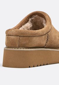 Scarpa slip-on in suede beige con fodera interna morbida, suola piatta spessa e cuciture decorative lungo il bordo superiore.