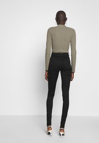 Mustat kapeat farkut korkealla vyötäröllä, yhdistettynä pitkähihaiseen raidalliseen puseroon oliivinvihreänä ja kermana. Ominaisuuksia ovat sileä pinta ja sulava istuvuus.