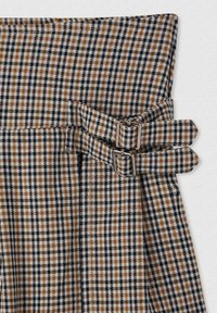 Tessuto a quadretti marrone, nero e bianco con una coppia di fibbie metalliche su una cintura piegata. Tessuto morbido con una forma strutturata.