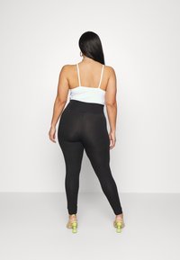 Leggings noirs taille haute au texture lisse associés à un top blanc à bretelles spaghetti ; portés avec des sandales à talon bloc transparent.