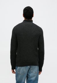 Tumehall maalritud kampsun kõrge krae ja soonilise tekstuuriga, millel on raglaanvarrukad ja vormitud taljeosa. Kandmisvalmis helesiniste teksadega.