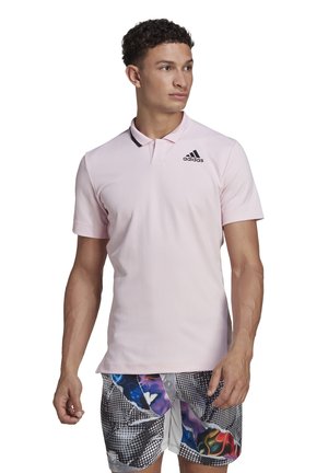 Polo shirt rose clair avec un design texturé, col côtelé et logo Adidas noir sur la poitrine gauche. Assorti à un short à motifs colorés.