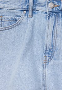 Vaaleansiniset farkut, joissa on hieno tekstuuri, ja jotka sisältävät yhden etutaskun, nappikiinnityksen sekä näkyviä ylitikkauksia saumoissa.