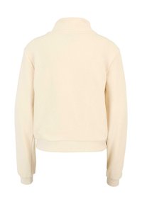 Pulover s crew-neck izduženih rukava u svijetlo bež boji, s mekom teksturom i rebrastim manžetama i donjim rubom. Jednostavan, neukrašen dizajn.