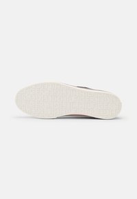 Schwarzer Sneaker mit einer weißen Gummisohle, der über eine geprägte Markenkennzeichnung verfügt. Glattes Obermaterial mit strukturierten Akzenten an den Seiten.