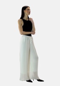 Pantaloni bianchi plissettati con vita elastica e dettagli con cordino, abbinati a un top aderente senza maniche di colore nero.