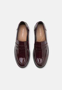 Burgunderfarbene Lacklederslipper mit glatter Textur, runder Zehenform und einem dekorativen Riemen über der Vorderseite. Schwarze Gummisohle.