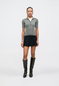 Gray ribbed polo shirt with short sleeves, paired with a black pleated skirt and knee-high black boots. Simple, fitted design.