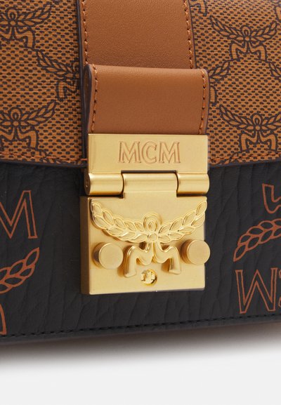 Gold clasp engraved with "MCM" and laurel emblem on brown and black textured leather with repeating logo pattern.