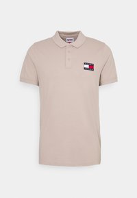 Beige pikétröja i bomull med krage, tre knappar och en färgglad logotyp på vänster bröst. Korta ärmar.