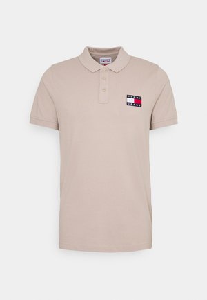 Beige polo shirt made of cotton, featuring a collared neck, three buttons, and a colorful logo patch on the left chest. Short sleeves.