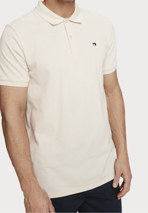 Polo-shirt i lys beige bomuld, kortærmet, med krave, der har et lille marineblåt logo på den øverste venstre bryst. Glat tekstur, klassisk pasform.