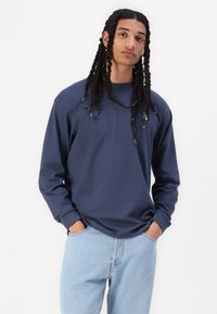 Navy long-sleeve shirt in soft cotton, featuring a relaxed fit and ribbed cuffs, paired with light blue denim jeans.