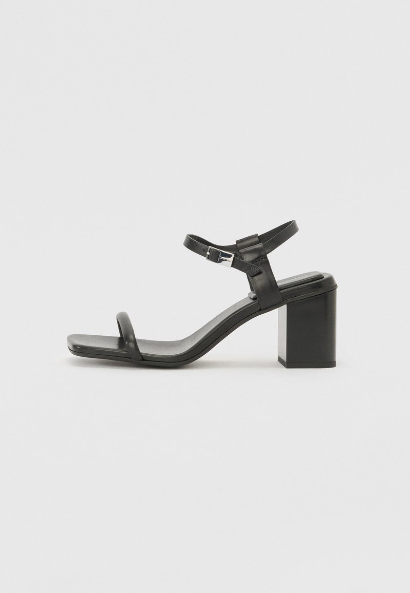 Black leather block-heeled sandal with a wide strap across the toe and an adjustable ankle strap, featuring a sleek, minimalist design.
