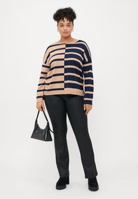 Striped sweater in beige and navy, featuring a color-block design, relaxed fit, and long sleeves. Paired with black, fitted pants and a small bag.