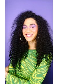 Grön tröja med virvlande gult mönster; lång, lockig svart hår; hoopörhängen; lila bakgrund; lila smink som framhäver ögonen.