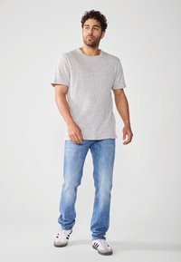 T-shirt grigio a maniche corte con un motivo a maglia testurizzato, abbinato a jeans dritti blu chiaro e sneakers bianche con strisce nere.