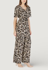 Mono con estampado de animales que presenta mangas cortas, cinturilla con lazo y piernas anchas en beige con patrones en negro y marrón. Combinado con tacones nude.