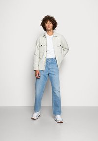 Lys grå skjorte med svarte detaljer, hvit t-skjorte, lyseblå rette jeans og hvite joggesko med brune såler.
