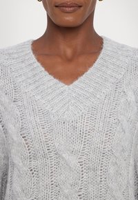 Light gray knitted sweater featuring a V-neck, cable knit design, and a slightly loose fit with a soft, fuzzy texture.