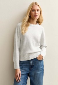 Helles graues, weiches Strickpullover mit Rundhalsausschnitt und geripptem Saum. Kombiniert mit blauen Jeans im entspannten Schnitt.