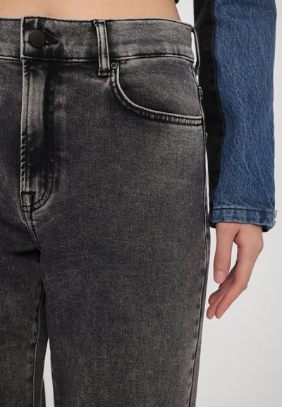 Faded black denim jeans with a slim fit, featuring front pockets and a button closure. Textured fabric with contrasting blue denim sleeve.