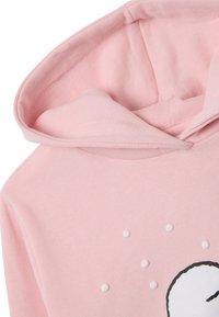 Felpa rosa con un texture morbido, una grande grafica con un design di volto semplice e punti bianchi sopra il volto.