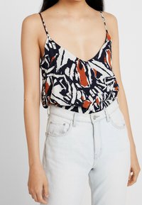 Multifarvet ærmeløs top med en dyb V-hals, prydet med et abstrakt mønster i marineblå, hvid og rustfarvet. Letvægtsmateriale med en afslappet pasform.