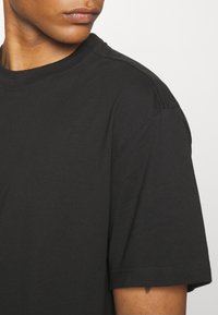 Czarny bawełniany T-shirt z okrągłym dekoltem, krótkim rękawem i luźnym krojem. Widoczne szwy na ramieniu. Miękka tekstura.