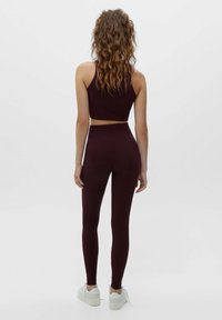 Ensemble coordonné en bordeaux comprenant un crop top et un legging en tissu extensible, avec une coupe ajustée et une texture unie, associé à des baskets blanches.