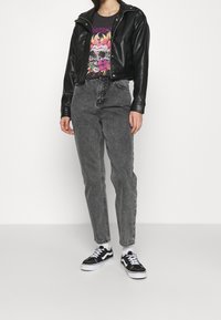 Chaqueta de cuero negra recortada sobre una camiseta gráfica con diseño de calavera, combinada con jeans de cintura alta grises y zapatillas en blanco y negro.