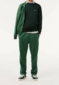 Grünes Sportoutfit bestehend aus einer Reißverschlussjacke und passenden Hosen, hergestellt aus weichem Stoff mit gerippter Textur und weißen Paspelierungsdetails.