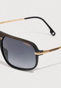 Črne in zlate sončne očala Carrera z gradientnimi temnimi lečami ter napisom "Carrera UV Protect" na leči in ročaju.