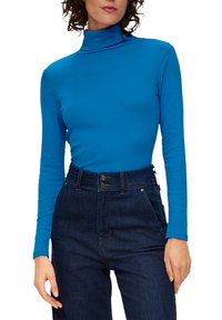 Turquoise lange-mouw turtleneck top gemaakt van gladde stof, gecombineerd met hooggewaist donkere jeans van denim met knopenaccenten.
