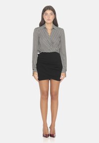 Blusa avvolgente a maniche lunghe con motivo bianco e nero, abbinata a una mini gonna nera e scarpe col tacco borgogna.