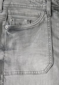 Lichtgrijze denim jeans met vijf zakken, contrasterende stiksels en een iets versleten textuur rond de achterzak.