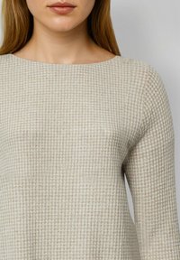 Jasnobeżowy sweter z teksturowanym wzorem w kratę. Posiada szeroki dekolt i długie rękawy, wykonany z miękkiego, dzianinowego materiału.