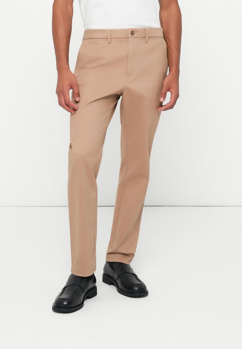 Beige bukser laget av lett stoff, med rett ben-design og frontlommer, kombinert med svarte loafers.