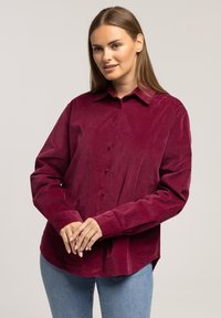 Burgundowa koszula z sztruksu z długimi rękawami, zapinana na guziki, z klasycznym kołnierzykiem. Gładka faktura i luźny krój.