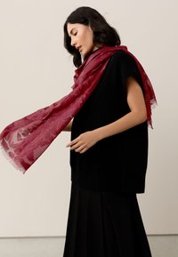 Black knitted oversized sweater with short sleeves worn with a sheer burgundy scarf featuring a subtle pattern, gently draped and flowing.