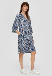 Blumenkleid mit Kragen, ¾-Ärmeln und seitlichen Taschen. Verfügt über blau, schwarz und rosa Muster auf einem hellen Hintergrund.